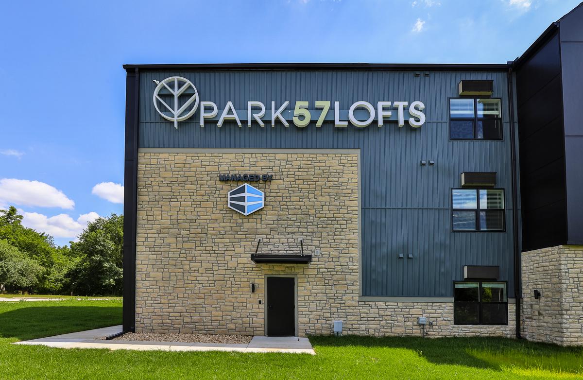 Close view of the PARK57LOFTS sign and leaf mark on the stone-and-siding gable, with the Managed By plaque