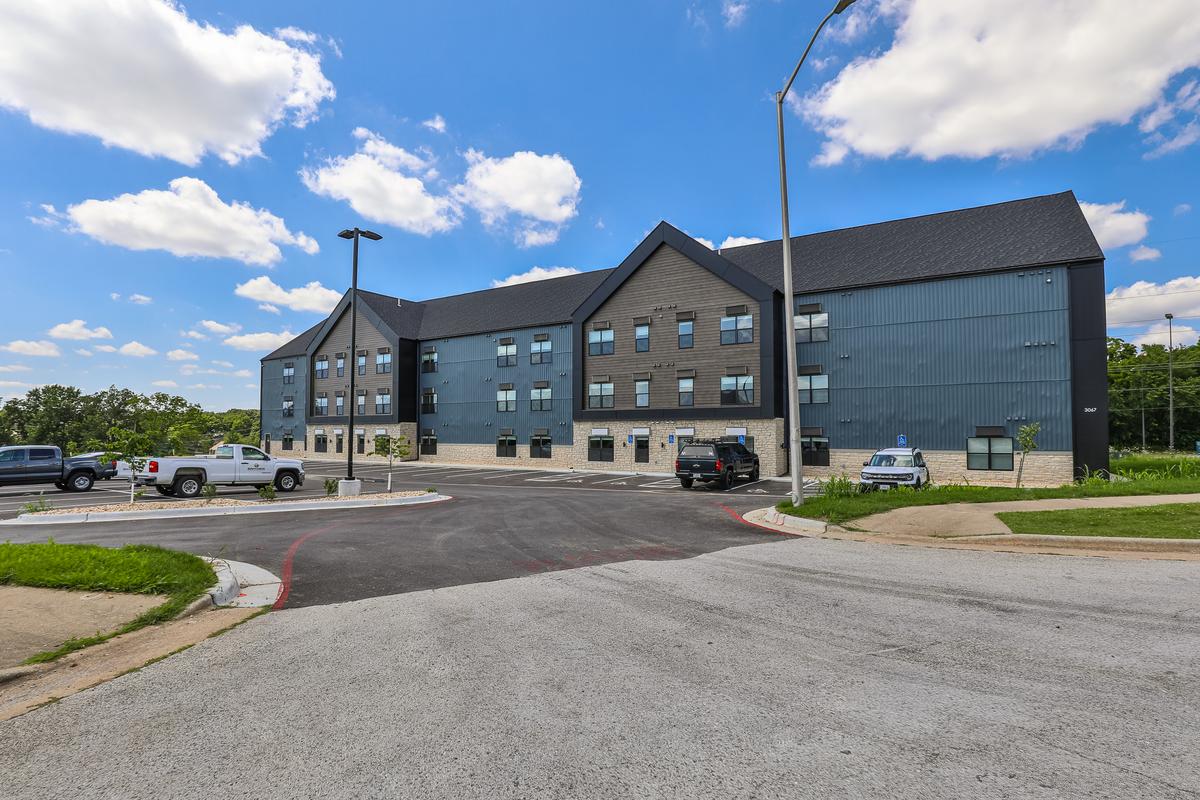 Wide view of the building across the parking lot and drive, lamp posts, clouds