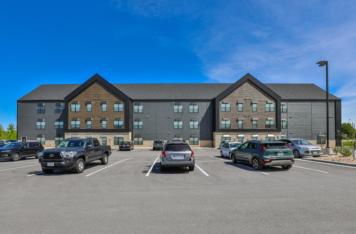 Front elevation from the parking lot: three gables, wood and blue-grey siding, cars parked